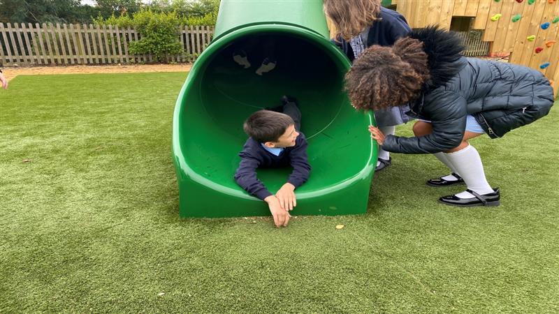 a child lies on his front at the bottom of the slide chatting to his friend 