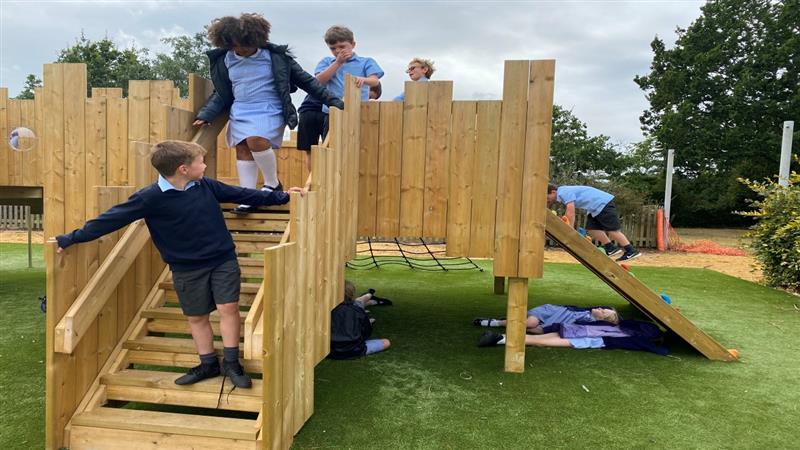children go down the timber steps of the langley play castle onto the green artificial grass turf below
