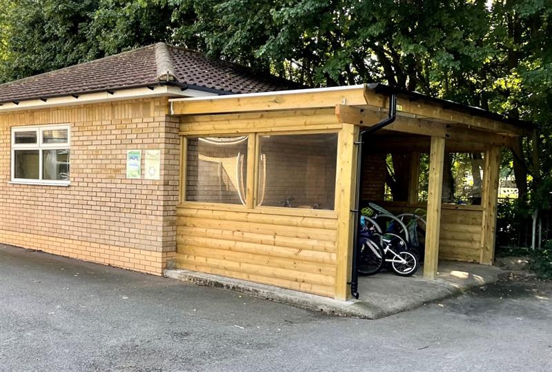 a timber bike shed at the side of the school building, including windows.