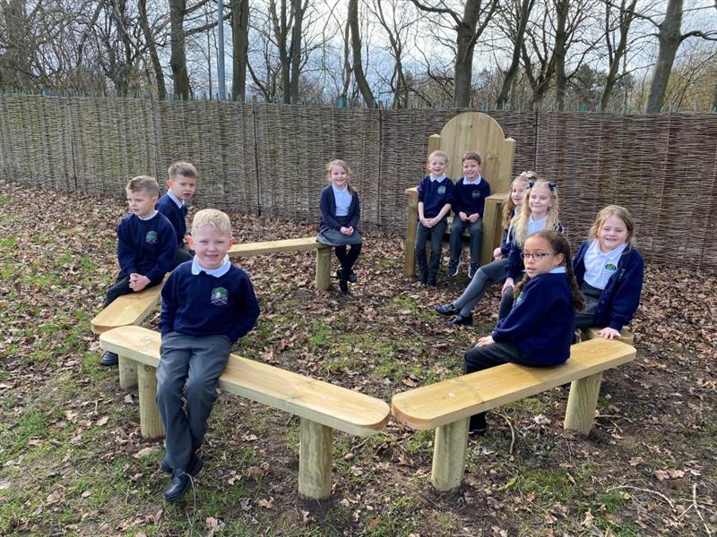 children sit on the perch benches in the story telling circle and smile at the camera