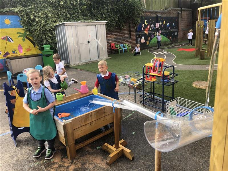 children play with the water table and the water channel stands whilst wearing messy play aprons
