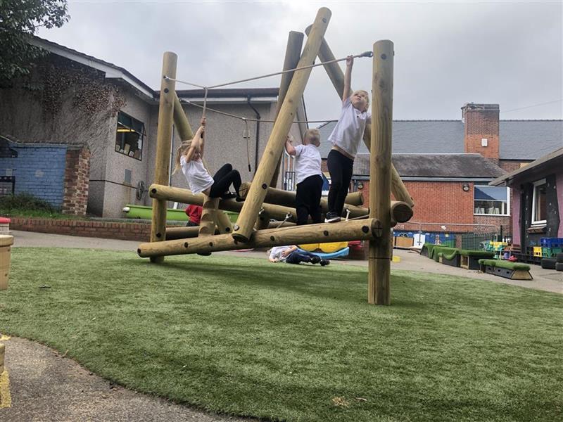 children in black and white school uniform climb on the harter fell climbing frame made from timber with artficial grass playurf
