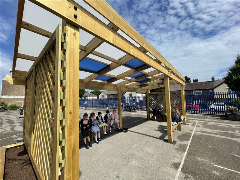 a side view of the timber canopy with blue and white polycarbonate roof tiles whilst children read books under the canopy