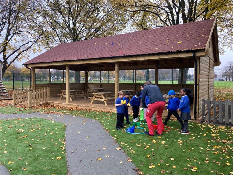 children in blue and black school uniform gather in a semi-circle on the green artificial playturf whilst talking to a teacher who is wearing red trousers 