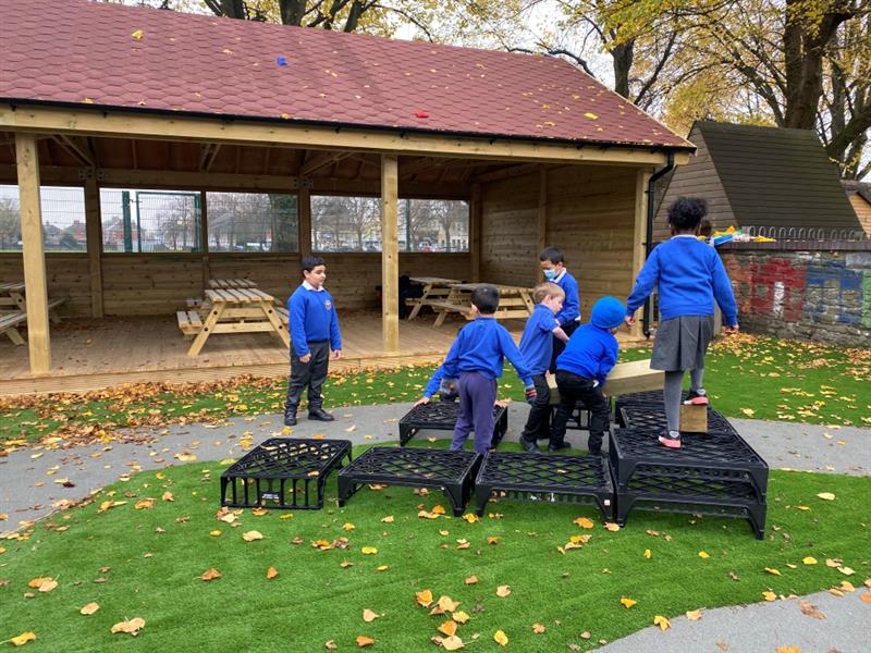 children play on the crates that they have placed on the green artificial grass surfacing 