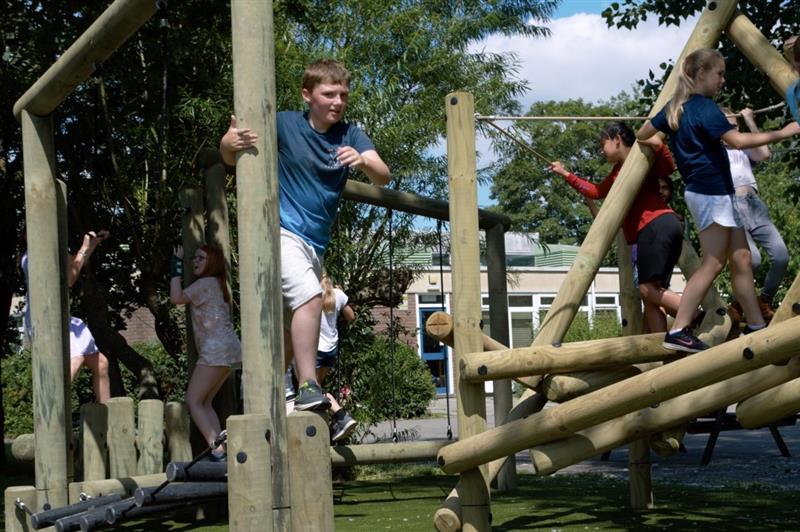 a little boy in white shorts and a blue t-shirt crosses the forest trim rail items and goes to jump of the end whilst looking at the camera