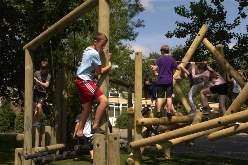 a child crosses the rubber stepping logs whilst children in the background play on the timber tryfan climber 