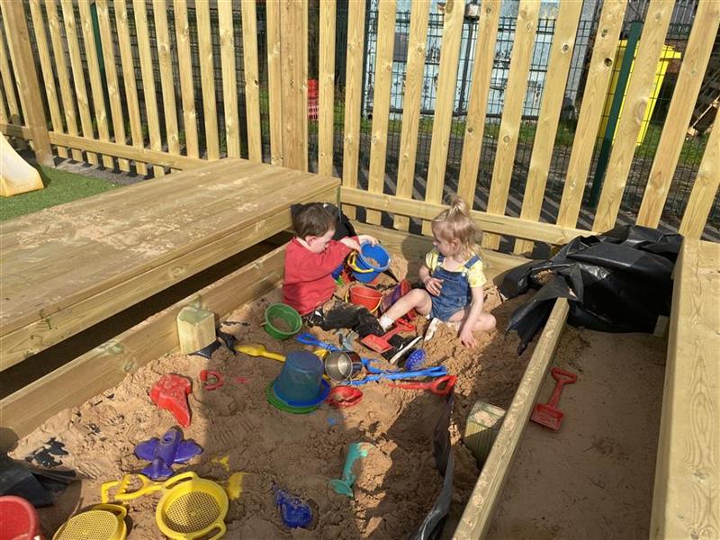 2 young children sat in the sand box with buckets and spades