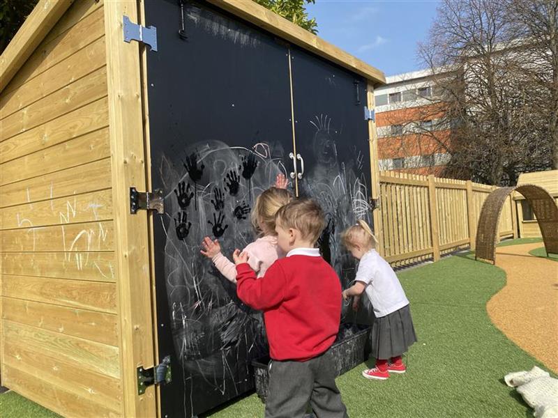 3 children playing on the chalk board on the storage unit