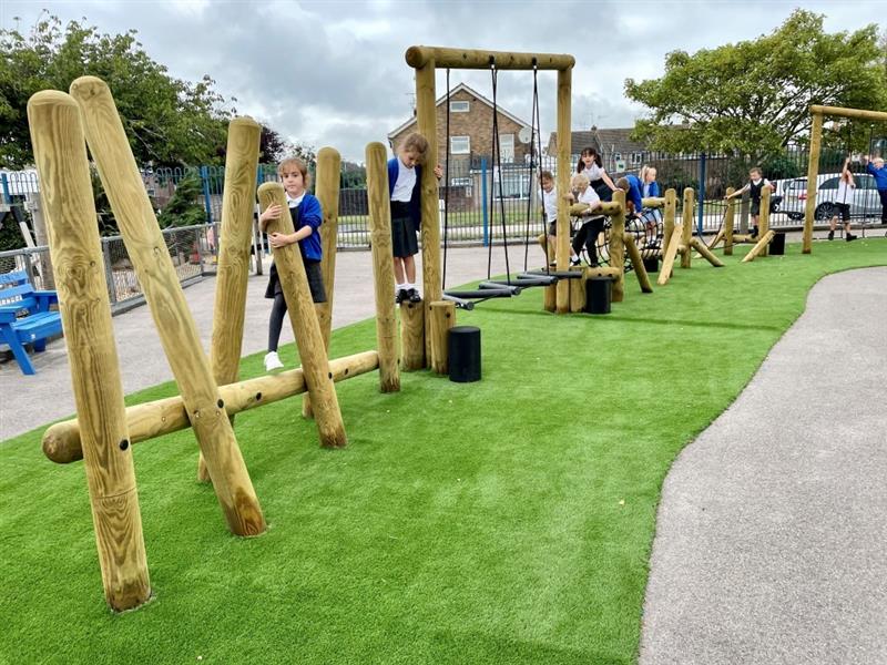 A class of children playing on the trim trail. Artificial grass surrounds the area.