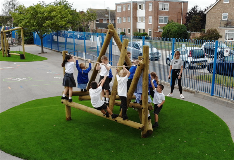 A class of children all climbing on the Harterfell climbing frame at their school.
