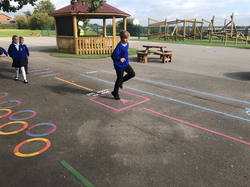 a child in blue and black school uniform plays on the fitness markings by hopping on the pink hop square as part of the fitness trail