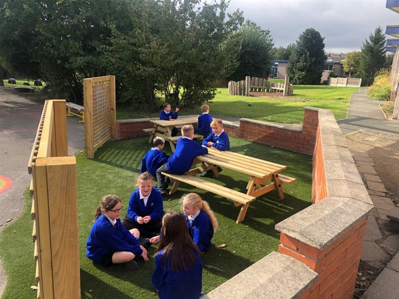 children sit on both the artificial grass and at the timber picnic tables 