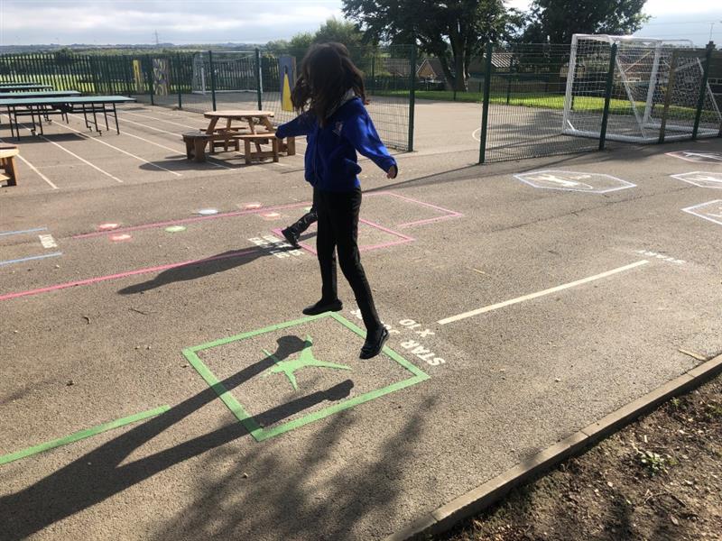 a child in blue and black school uniform does a star jump on the star jump playground marking