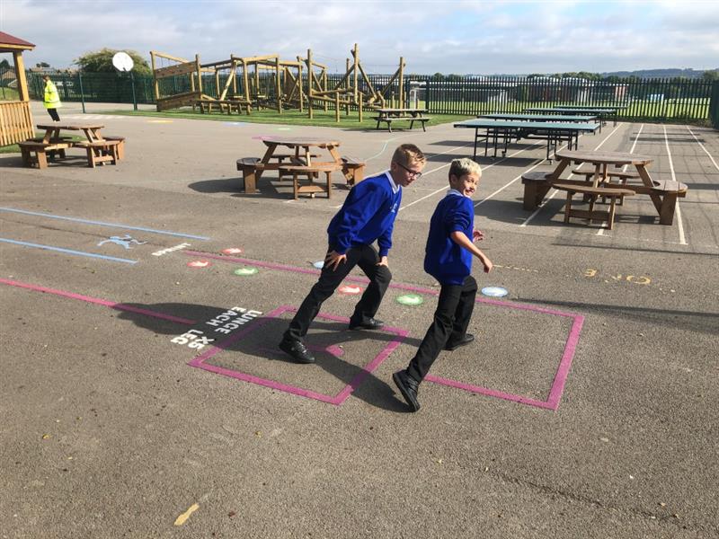 two little boys in blue, white and black school uniform run around on the pink playground markings 