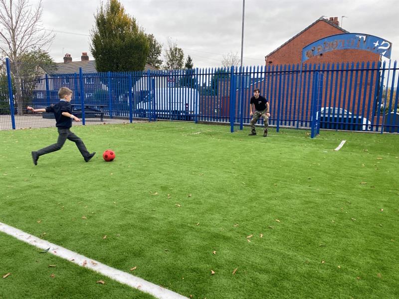 a child aims at the goal whilst some stands as the goal keeper ont he new muga with surfacing
