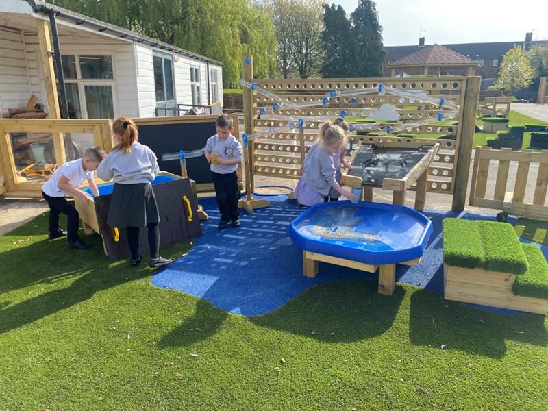 children stand in the water zone and play with the water table, tuff spot table, water wall and damming station