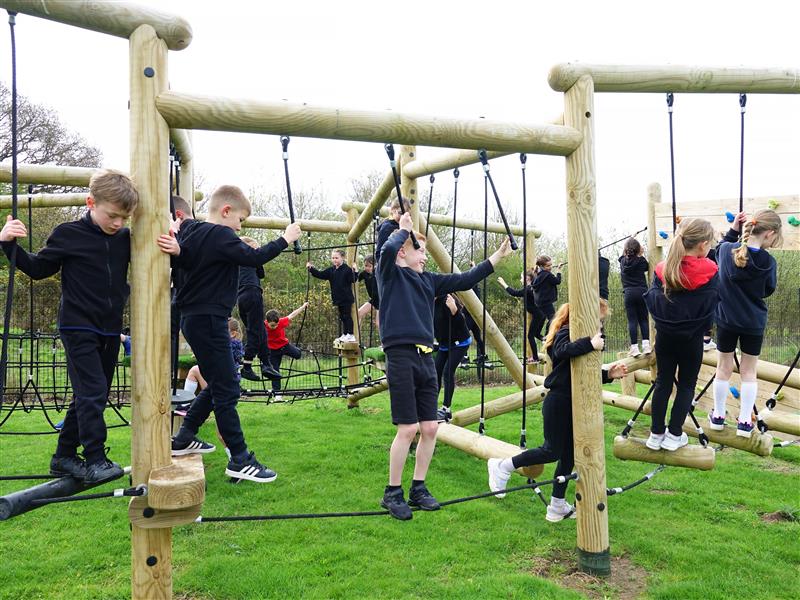 A class of children climbing across the climbing frame in their playground 