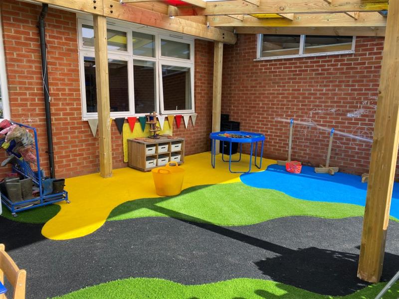 a blue tuff spot table sits in the corner of the timber canopy with yellow, blue, green and black saferturf surfacing under the timber bespoke canopy