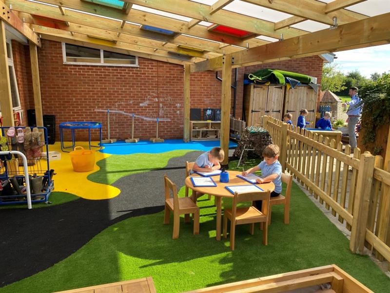 two little boys in blue and black school uniform sit at a table under the bespoke timber canopy with the multi-coloured surfacing in the background