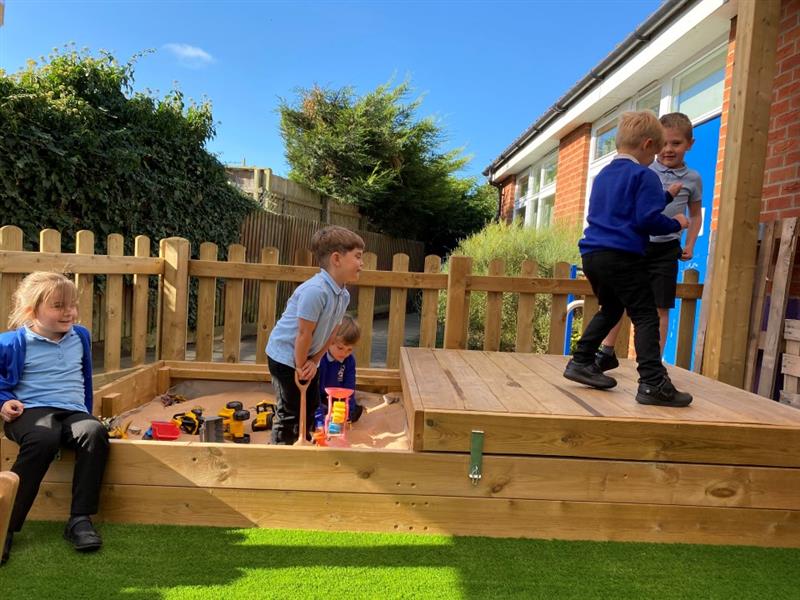 children in blue and black school uniform stand on the sliding sandpit roof using it as a stage and playing with the sand that is still out on one side