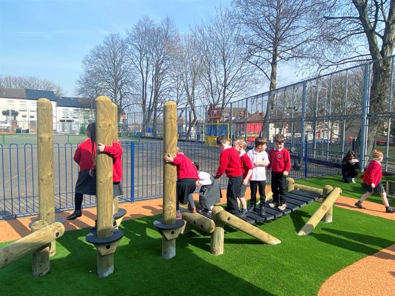 children in red, white and grey uniforms cross the clatter bridge, disc poles and the balance beam