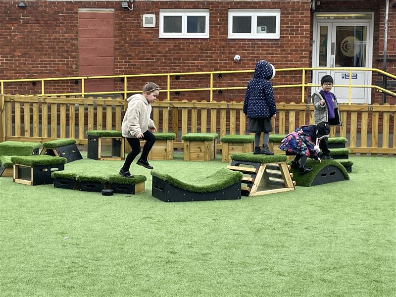 a class of children playing on the artificial grass top blocks 