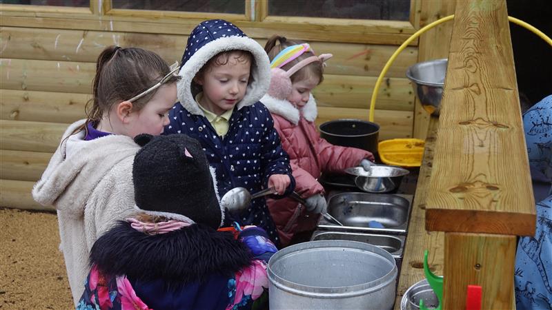 A class of children playing in the mud on the mud kitchen