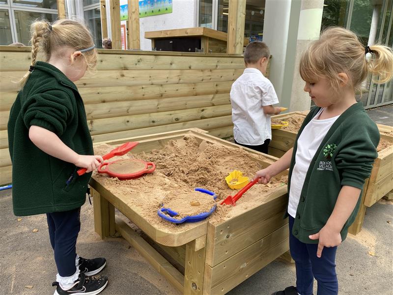 children stand aroudn the sand table and dig into it using the shovels