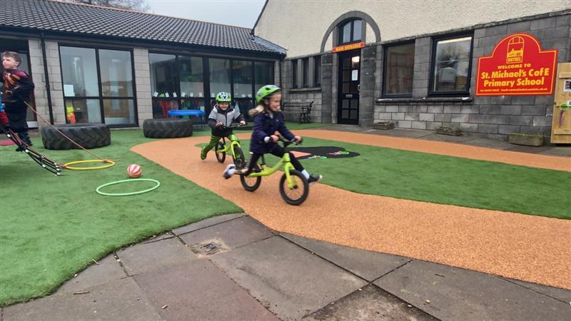 children scoot around on the beige wetpour on their scooters