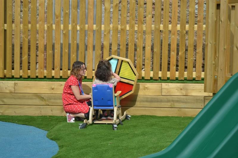 a teacher kneels on artificial grass next to a child playing with the sensory spinner