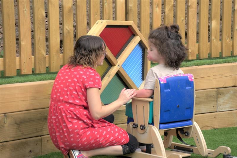 a little girl sits in front of the sensory spinner and plays with the teachers' support