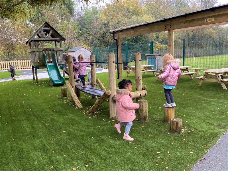 the timber canopy in the background behind the clatter bridge with artificial green grass surfacing beneath as children queue to go on the bridge