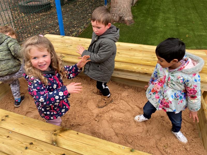 four children in winter coats sit in the sand box and play with the sand 