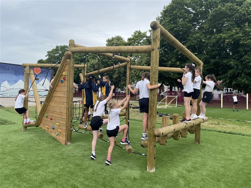 Children in black and white pe kit climb on the timber climbing frame