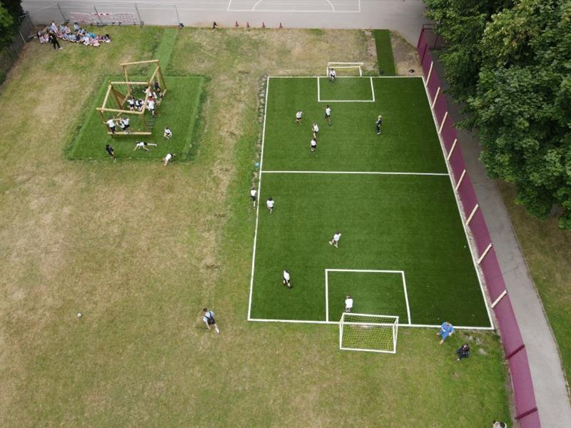 a birdseye view of the green muga with white lines that children are playing a game of football on