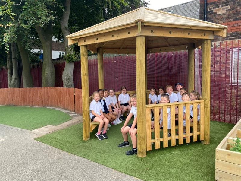 children sit together in the hexagonal gazebo and smile at the camera