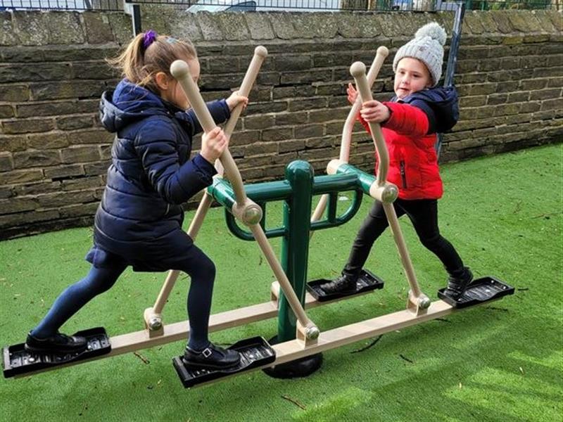 2 young girls playing on a piece of the outdoor gym equipment at the primary school.