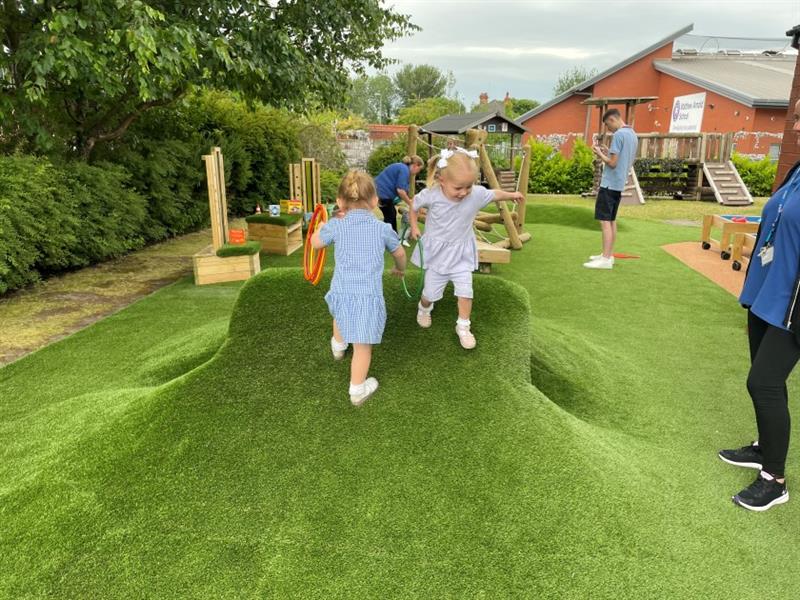 children run over the playground mounds in the artificial grass and the tunnel hill