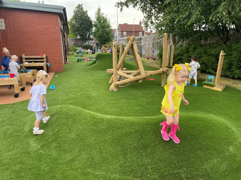 two little girls run over the playground mounds on the ground underneath the artificial grass