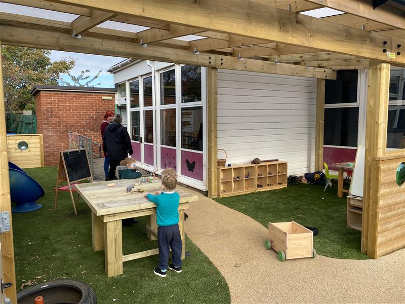 children playing on a table uderneath an outdoor classroom canopy