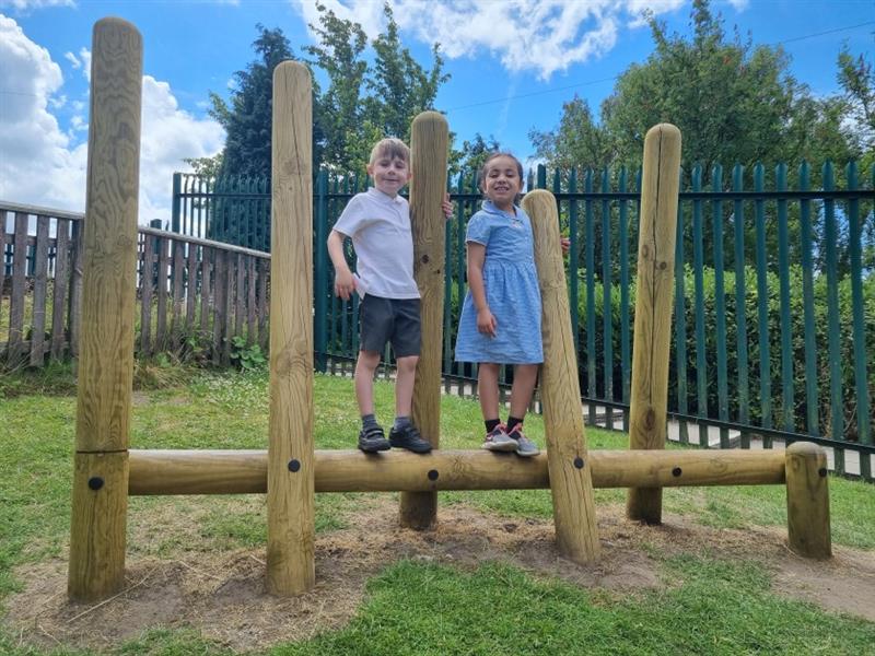 two children walk along he log balance weaver and smile at the camera