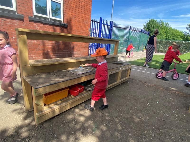 a child stands and plays with the mud kitchen on a sunny day