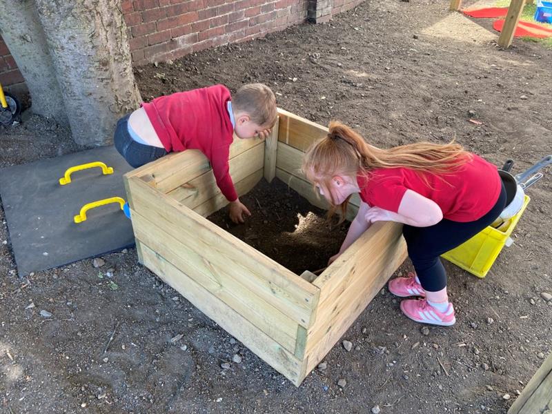 two children lean into the mud box and dig around for mud to play on the kitchen with