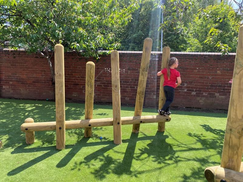 a child crosses the log balance weaver with the green grass surfacing below