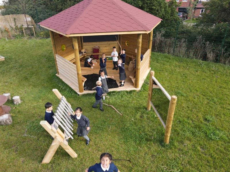 children play in the sensory gazebo and with musical instruments and look up at the drone flying above them as they smile and laugh