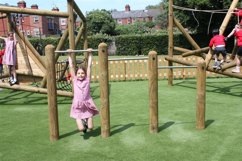 s child swings on the timber and metal forest pull up and rollover bars as she smiles at the camera