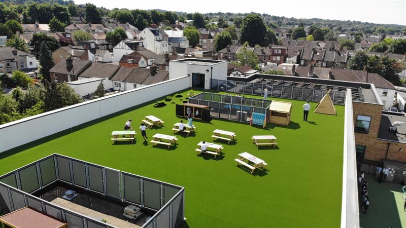 A birds eye view of the library in the sky playground, with 8 picnic benches on the artificial grass