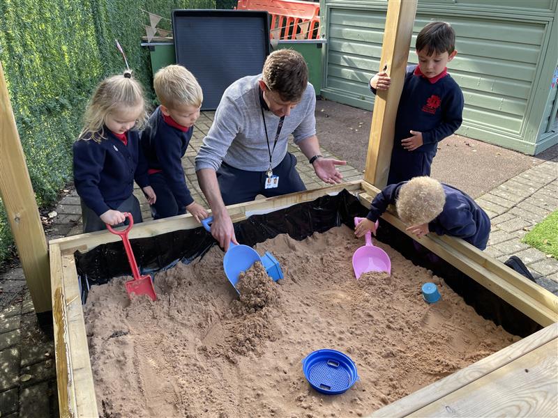 children sit around a sandpit and play with the materials