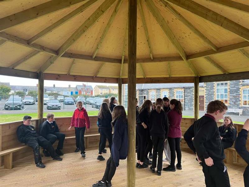 Inside the outdoor gazebo at this primary school, there are children sat on the benches around the gazebo
